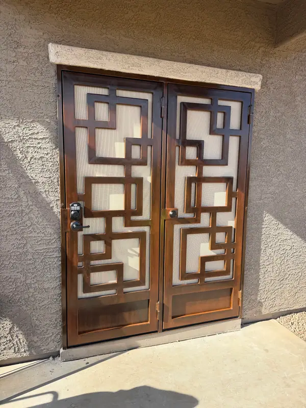 Double security doors with an interlocking squares pattern in a bronze finish at a stucco entry
