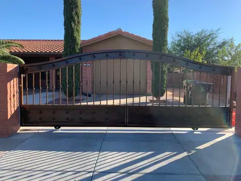 Arched rolling drive gate with bars and diamond accents across a driveway