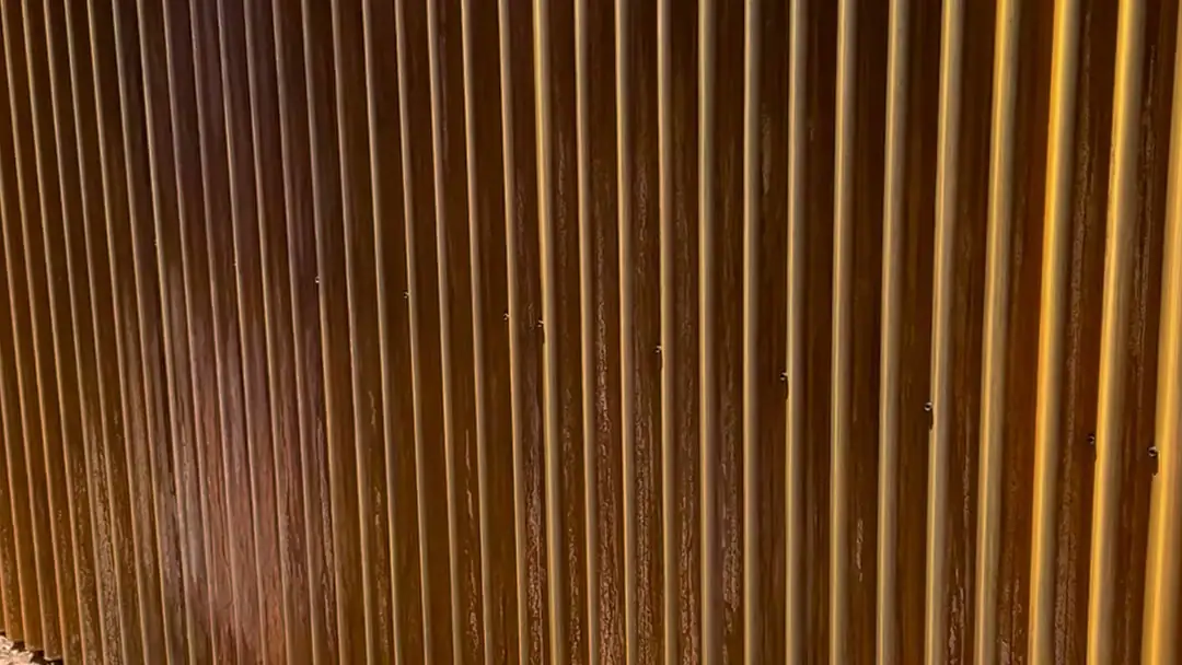 Rusted corrugated steel fence built by Nunez Welding, beside a saguaro in a Tucson yard