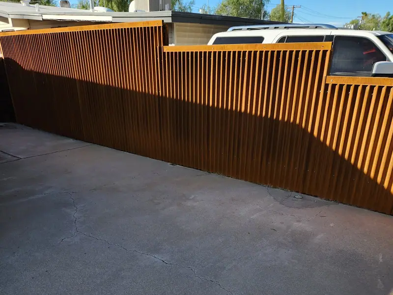 Rusted corrugated steel fence with a raked top running along a driveway